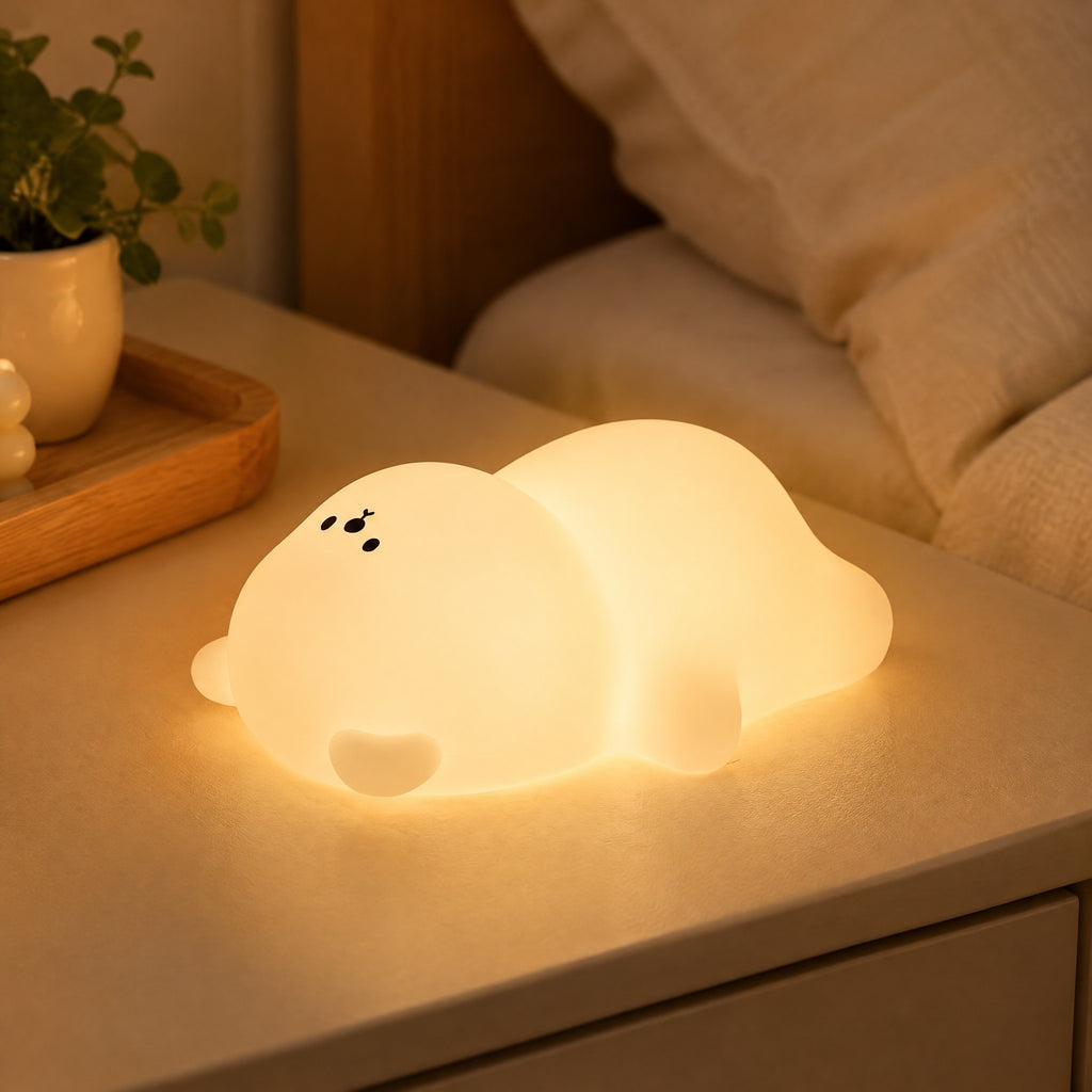 Veilleuse ourson en silicone blanche allumée sur une table de chevet beige
