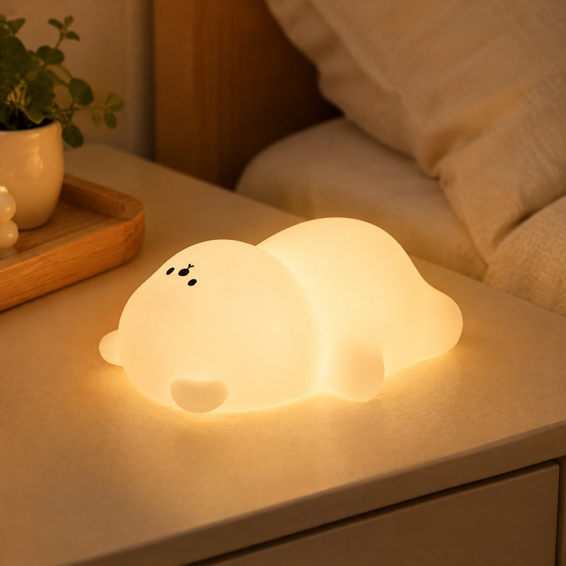 Veilleuse ourson en silicone blanche allumée sur une table de chevet beige