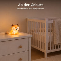 Eingeschaltetes Fuchs-Nachtlicht auf einer Kommode im Babyzimmer neben einem Gitterbett