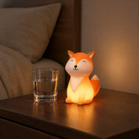 Lit orange fox night light on a bedside table next to a glass of water