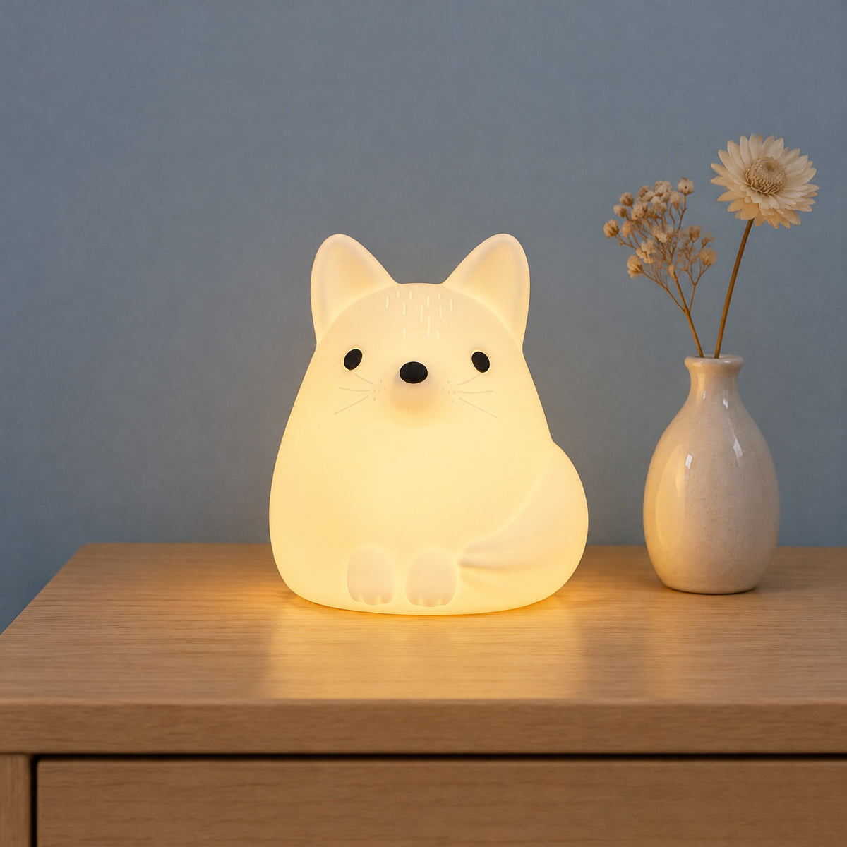 Fuchs-Nachtlicht in Weiß eingeschaltet auf einer Kommode vor einer blaugrauen Wand, mit einer kleinen Vase mit Trockenblumen